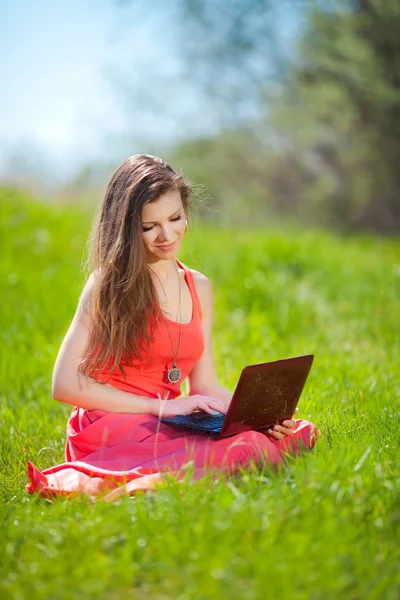 Retrato de uma jovem mulher inteligente deitada na grama e usando laptop — Fotografia de Stock