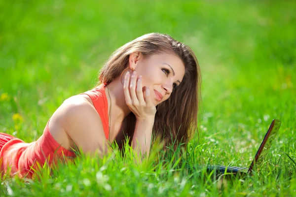 Portrait of a smart young woman lying on grass and using laptop — Stock Photo, Image