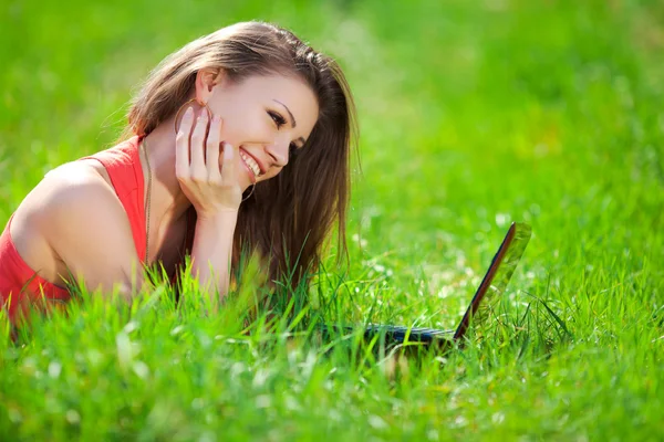 Retrato de uma jovem mulher inteligente deitada na grama e usando laptop — Fotografia de Stock