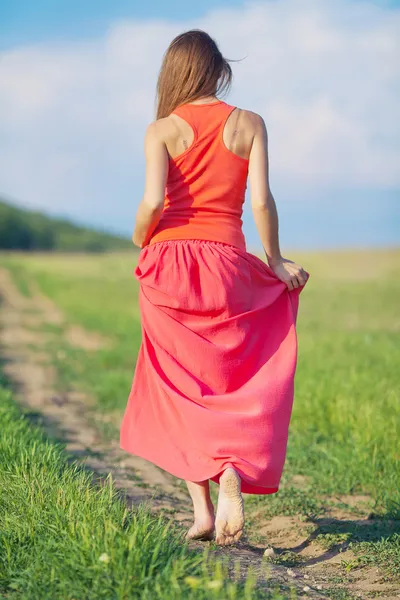 Portrait of a beautiful young woman in a red dress on a background of sky and grass in summer