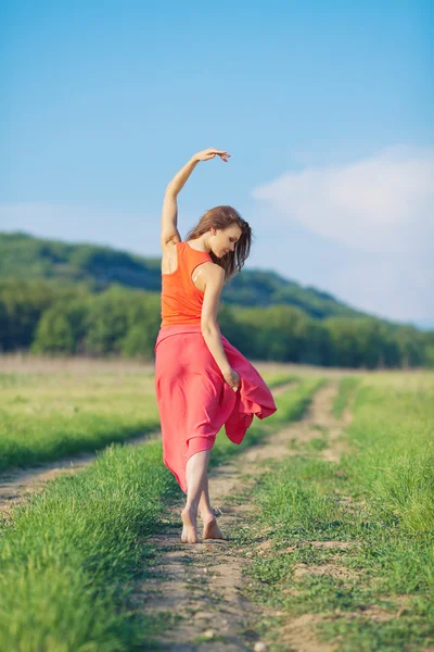 Portrait of a beautiful young woman in a red dress on a background of sky and grass in summer — Stock Photo, Image