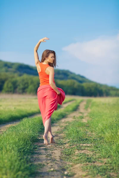 Portrait of a beautiful young woman in a red dress on a background of sky and grass in summer — Stock Photo, Image