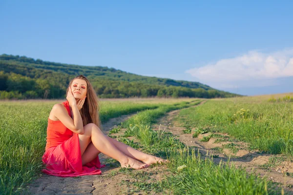 하늘의 배경에 빨간 드레스에 아름 다운 젊은 여자와 여름에는 잔디의 초상화 — 스톡 사진