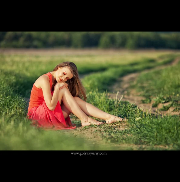 Portret to piękna młoda kobieta w czerwonej sukience na tle nieba i trawa w lecie — Zdjęcie stockowe