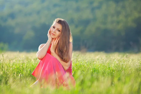 Retrato de uma bela jovem mulher em um vestido vermelho em um fundo de céu e grama no verão — Fotografia de Stock