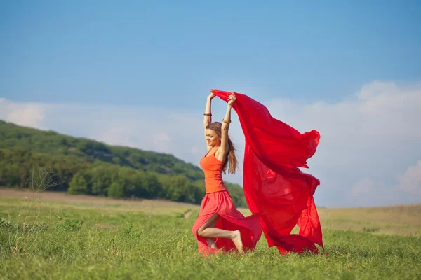 Ritratto di una bella giovane donna vestita di rosso su uno sfondo di cielo ed erba in estate — Foto Stock