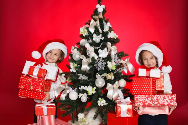 Portrait de Santa chapeau filles de Noël tenant cadeaux de Noël souriant heureux et excité. Mignon beau père Noël enfants sur fond rouge . — Photo