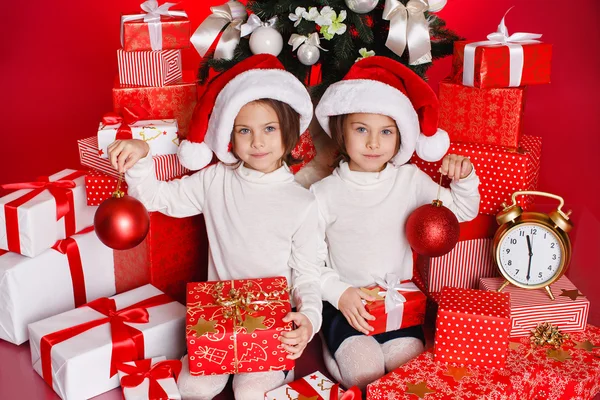 Ritratto di Babbo Natale cappello ragazze che tengono regali di Natale sorridente felice ed eccitato. Carino bei bambini di Babbo Natale su sfondo rosso . — Foto Stock