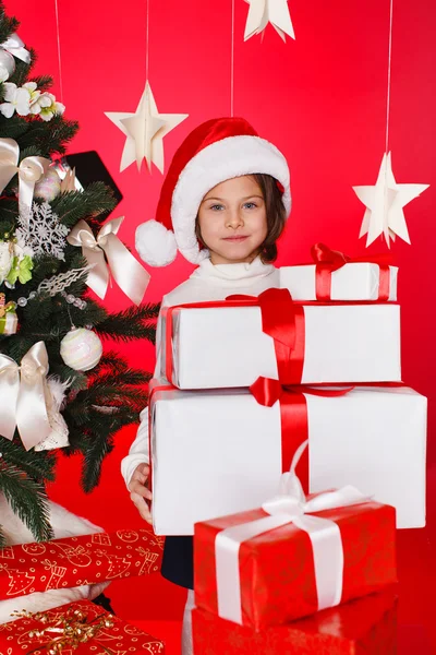 Porträtt av santa hatt jul tjejer hålla julklappar leende glad och upprymd. söt vackra santa barn på röd bakgrund. — Stockfoto