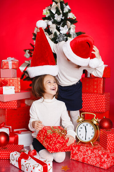 Portrait of Santa hat Christmas girls holding christmas gifts smiling happy and excited. Cute beautiful santa children on red background.