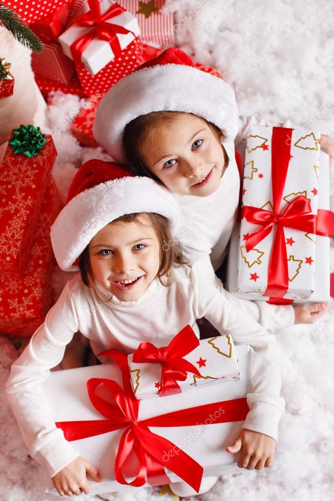 Portrait of Santa hat Christmas girls holding christmas gifts smiling happy and excited. Cute beautiful santa children on red background.