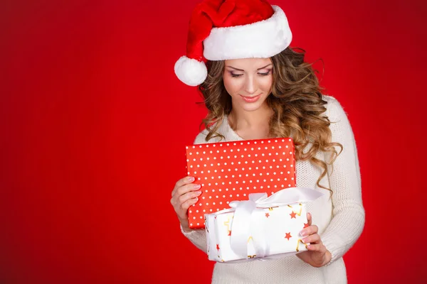 Santa flicka håller julklapp. glad ung kvinna i santa hat söker sidled visar julklapp isolerad på vit bakgrund. vacker söt ung kvinna som santa. — Stockfoto