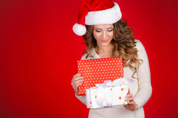 Santa girl holding christmas gift. Young happy woman in santa hat looking sideways showing Christmas present isolated on white background. Beautiful cute young santa woman.