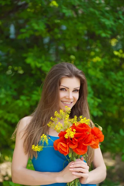 Porträtt av glad kvinna utomhus med röd vallmo blommor i händerna — Stockfoto