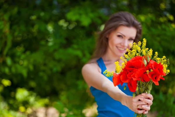 Porträtt av glad kvinna utomhus med röd vallmo blommor i händerna — Stockfoto