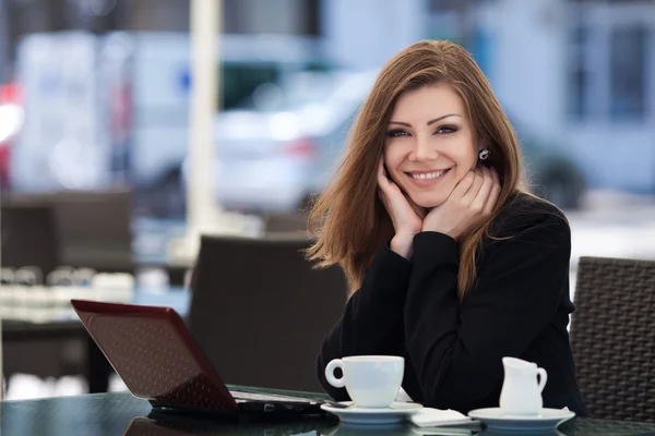 Portré, szép mosolygó nő ül egy laptop szabadtéri kávézóban — Stock Fotó