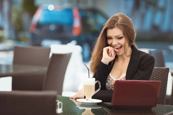 Retrato de una hermosa mujer sonriente sentada en un café con computadora portátil al aire libre — Foto de Stock