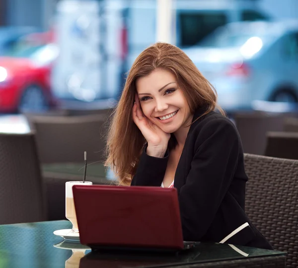 Портрет красивой улыбающейся женщины, сидящей в кафе с ноутбуком на открытом воздухе — стоковое фото