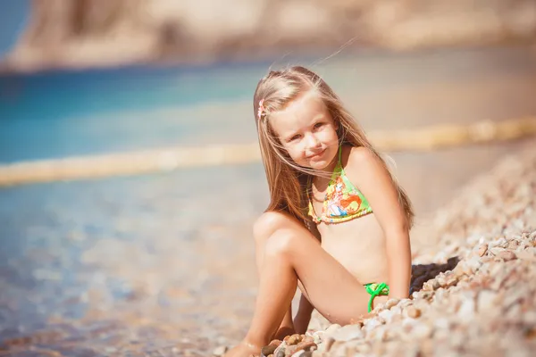 Niña sentada en la playa cerca del mar — Foto de Stock