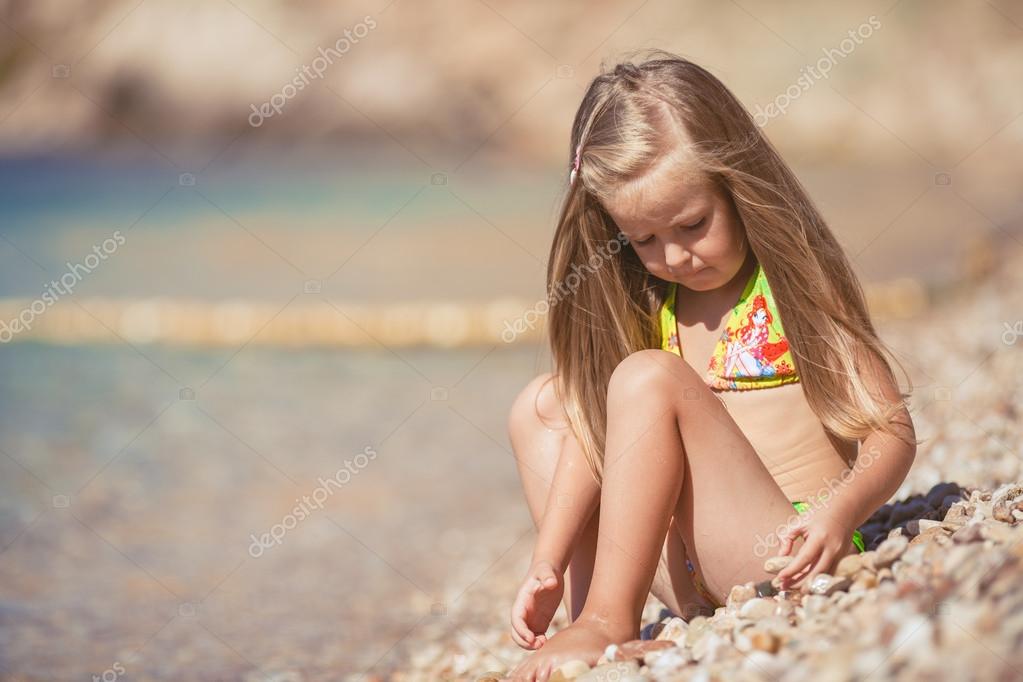 Little girl sitting on the beach near the sea Stock Photo by ©golyak
