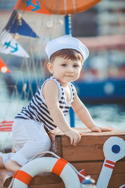 Menino bonito sentado no chão no cais ao ar livre, um estilo marinho. Pequeno marinheiro — Fotografia de Stock