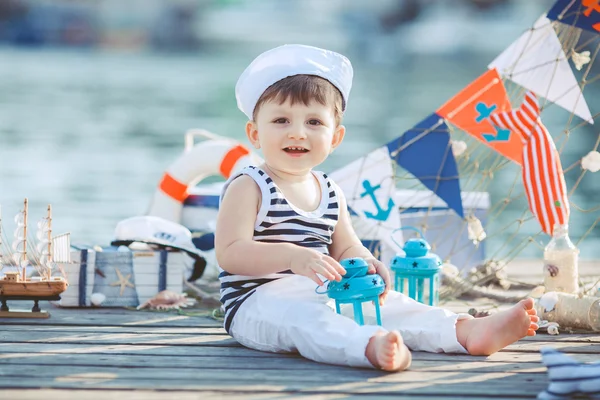 Menino bonito sentado no chão no cais ao ar livre, um estilo marinho. Pequeno marinheiro — Fotografia de Stock