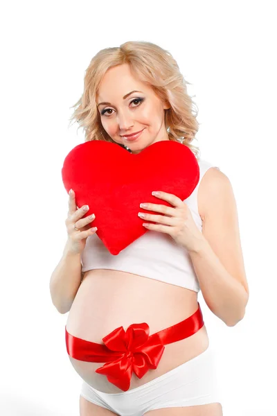 Pregnant beautiful woman holding red heart pillow in her hands isolated on white background — Stock Photo, Image