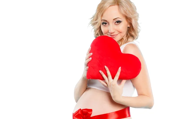 Pregnant beautiful woman holding red heart pillow in her hands isolated on white background — Stock Photo, Image