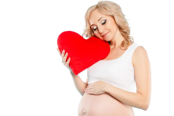 Беременная красивая женщина с красной подушкой сердца в руках изолированы на белом фоне — стоковое фото