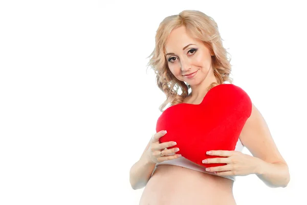 Pregnant beautiful woman holding red heart pillow in her hands isolated on white background — Stock Photo, Image