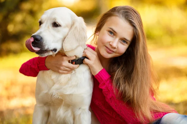 Portrait of Young girl sitting on the ground with her dog retriever in autumn scene — Stock Photo, Image