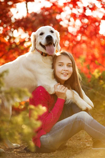 Portrait of Young girl sitting on the ground with her dog retriever in autumn scene — Stock Photo, Image