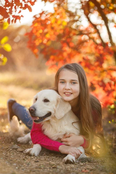 Портрет молодой девушки, сидящей на земле с собакой ретривер в осенней сцене — стоковое фото