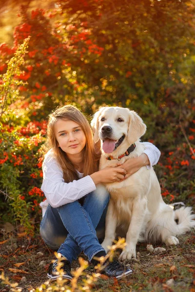 Portrait of Young girl sitting on the ground with her dog retriever in autumn scene — Stock Photo, Image