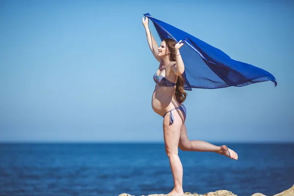 Mladá těhotná žena dýchá čerstvý mořský vzduch na pozadí hory — Stock fotografie