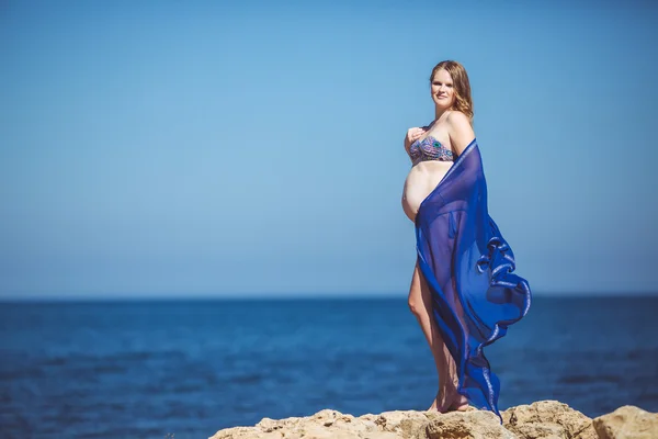 Молодая беременная женщина дышит свежим морским воздухом на фоне гор — стоковое фото