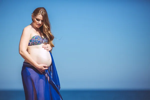 Young pregnant woman breathes the fresh sea air on a background of mountains