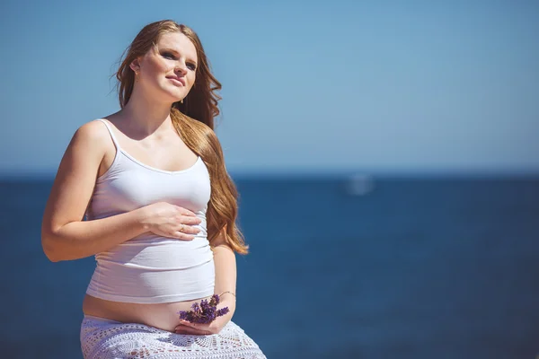 Young pregnant woman breathes the fresh sea air on a background of mountains — Stock Photo, Image