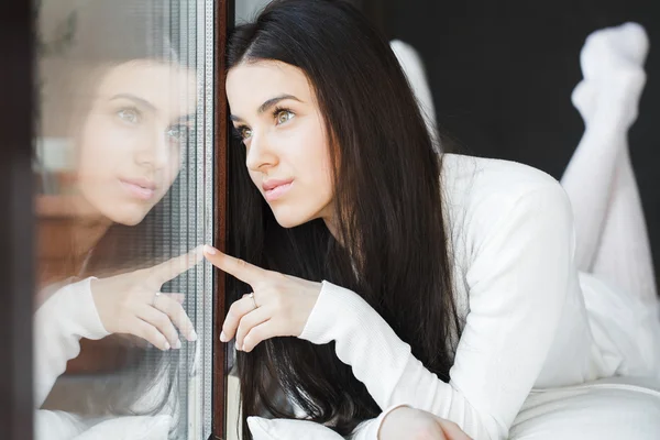 Retrato de una joven hermosa mujer sentada en el sofá en su habitación cerca de la ventana en blanco — Foto de Stock