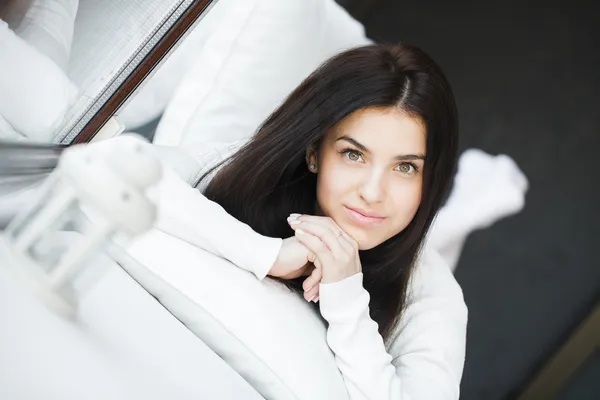 Retrato de una joven hermosa mujer sentada en el sofá en su habitación cerca de la ventana en blanco — Foto de Stock