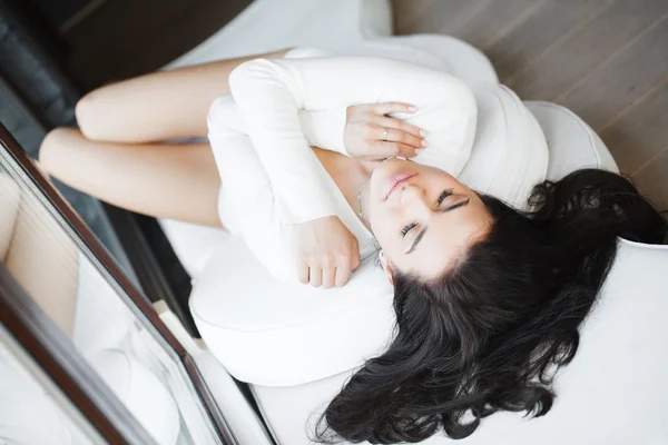 Portrait d'une jeune belle femme assise sur le canapé dans sa chambre près de la fenêtre en blanc — Photo