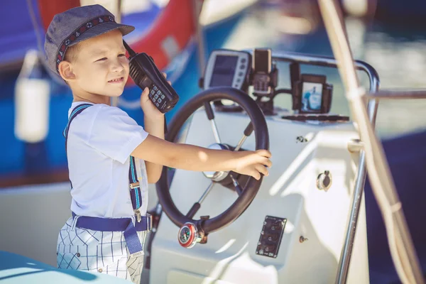 Söta lilla sailor boy har fan nära båtar på pier nära havet. utomhus. — Stockfoto