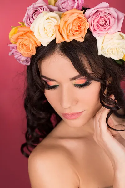 Retrato de belleza de una mujer con una corona de flores en la cabeza un fondo rojo —  Fotos de Stock