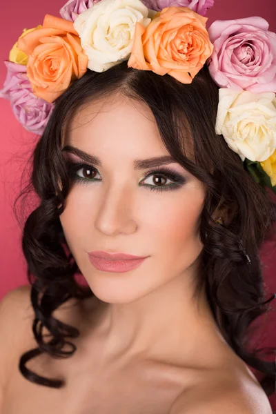 Hermosa morena mujer joven con corona de flores estudio tiro fondo rosa — Foto de Stock