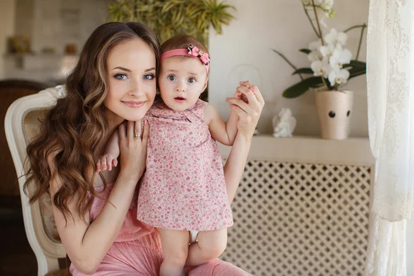 Retrato de jovem mãe atraente feliz brincando com sua menina perto da janela no interior no haome. Vestidos cor de rosa em mãe e filha — Fotografia de Stock