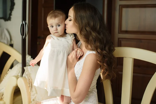 Portrait of happy young attractive mother playing with her baby girl near window in interior at haome. Pink dresses on mother and daughter — Stock Photo, Image