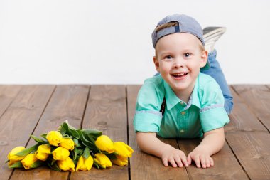 gülen çocuk ahşap yerde otururken elinde bir buket Sarı laleler holding