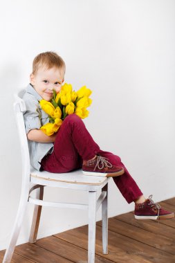 Portrait of Smiling boy with a bouquet of yellow tulips flowers in hands standing near white wall clipart
