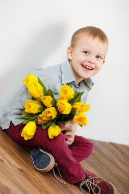 gülen çocuk ahşap yerde otururken elinde bir buket Sarı laleler holding