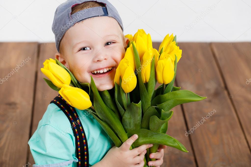 Smiling boy holding a bouquet of yellow tulips in hands sitting on wooden floor
